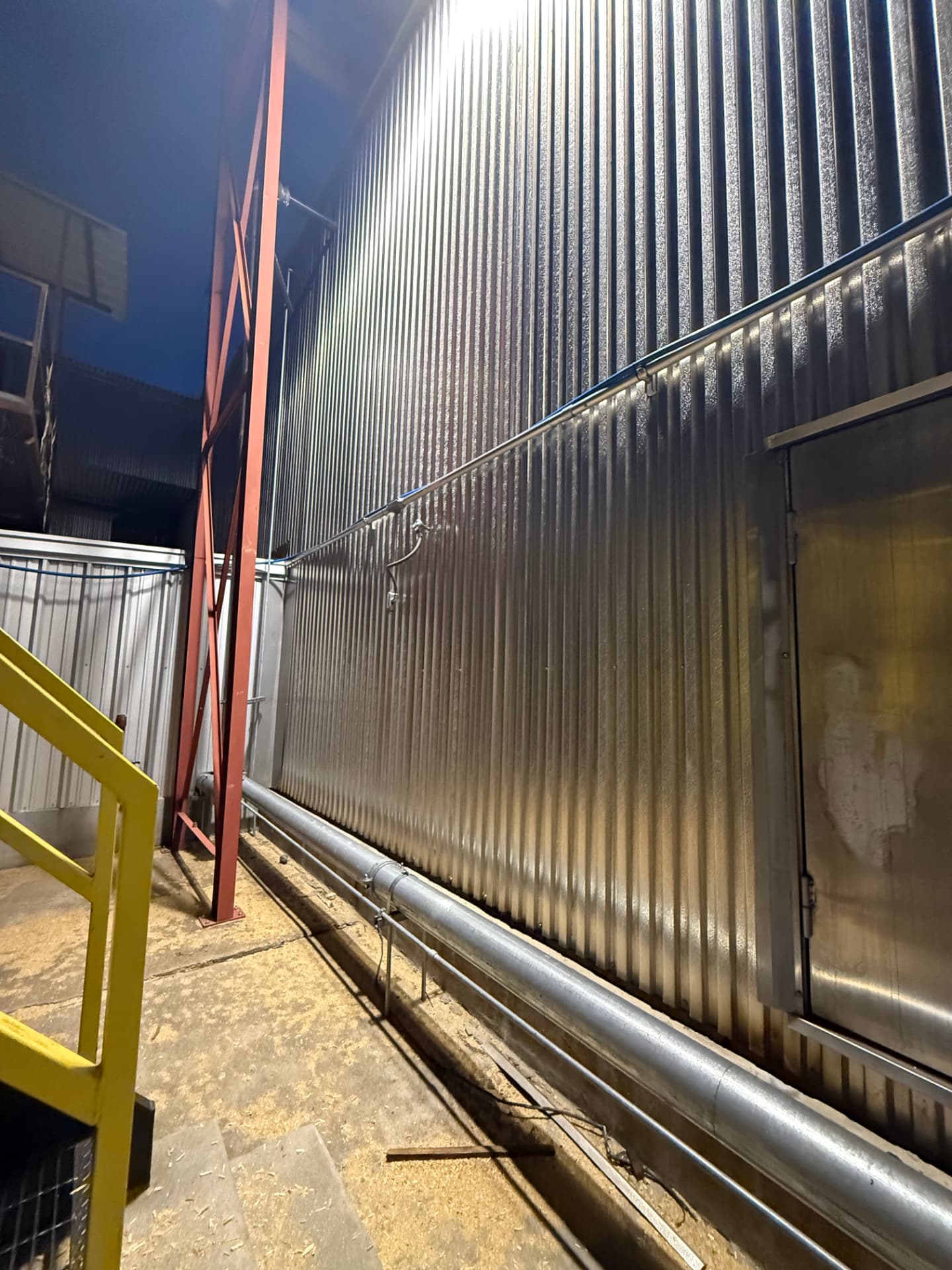 Dry kiln exterior wall with steam line and walk door at night
