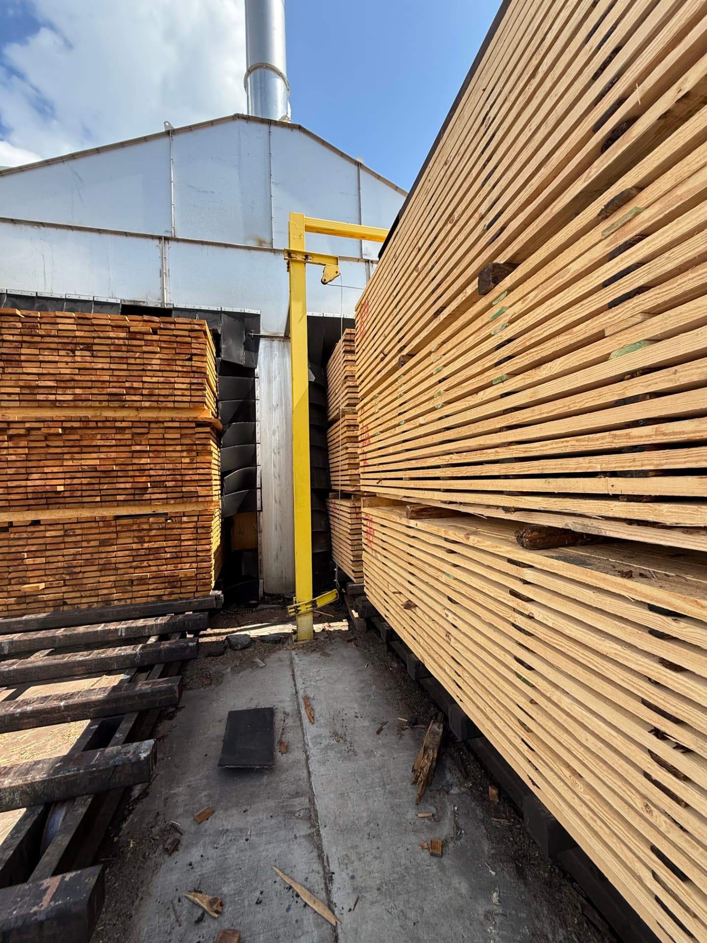 Stickered lumber charges staged beside a kiln fan wall at a sawmill